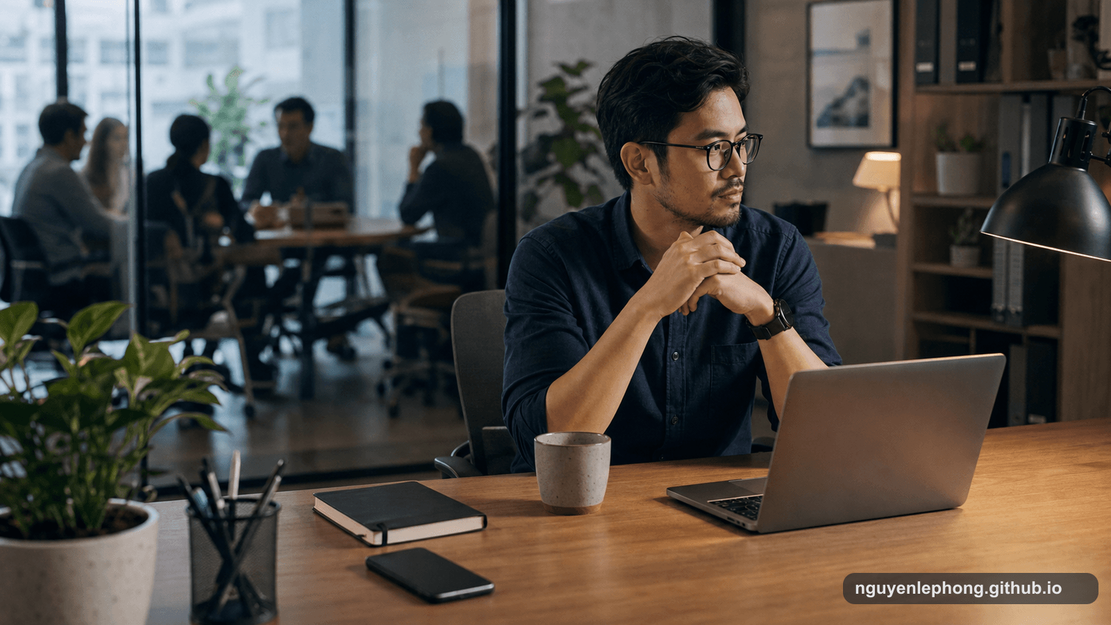 A Vietnamese professional sits quietly at a desk after a meeting, with a phone face down, a notebook, and coworkers blurred behind glass.