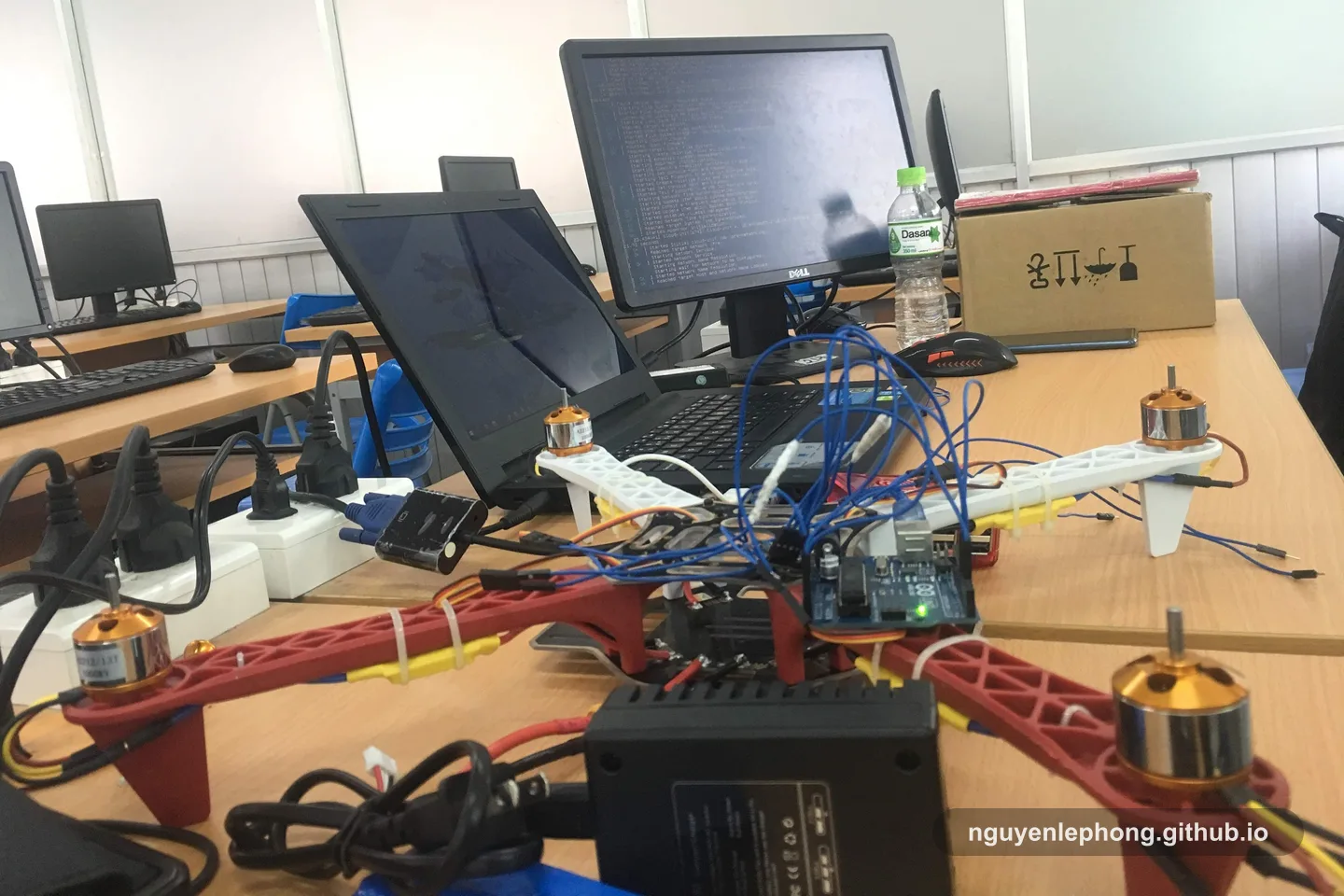 Một mẫu drone đặt trên bàn lab cạnh laptop, dây nối và bộ test sẵn để kiểm tra.