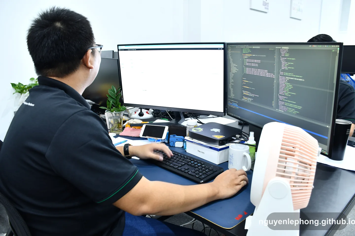 Nguyen Le Phong works at a cluttered desk with code open across two monitors, pausing to question the pattern in front of him.