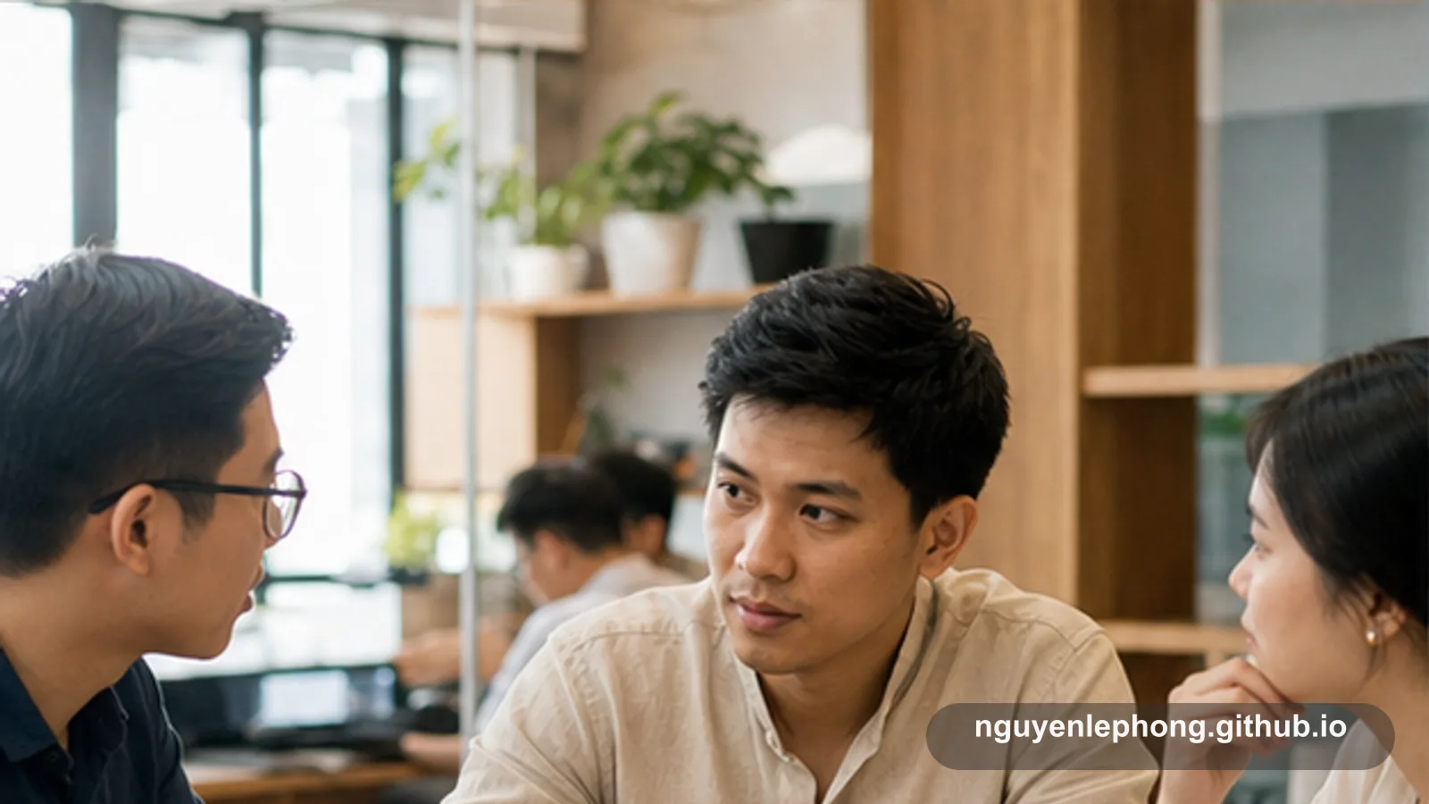 Ba đồng nghiệp ngồi gần nhau trong văn phòng; người ở giữa nhìn sang người bên trái khi cả nhóm đang trao đổi.
